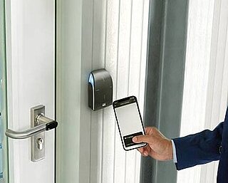 Man stands in front of the door and holds his smartphone to the reader for mobile access control.